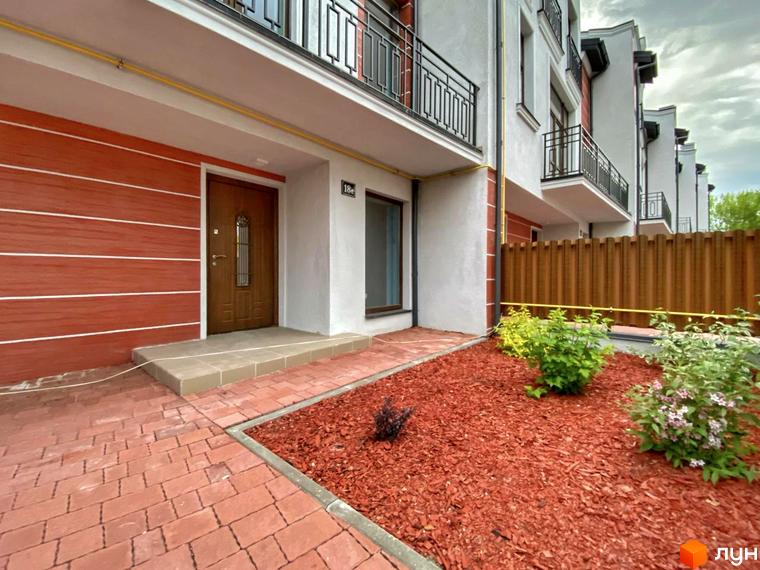 Фасад таунхауса в Raytman Park. Двоповерховий будинок з балконами та червоною цегляною кладкою, перед будинком газон з декоративною мульчею.