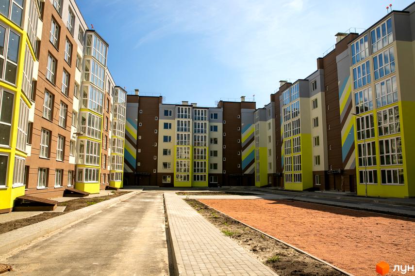 Зовнішній вигляд новобудови ЖК Welcome Home на Стеценка з яскравими фасадами та скляними балконами. Прибудинкова територія з пішохідними доріжками та піщаною зоною.