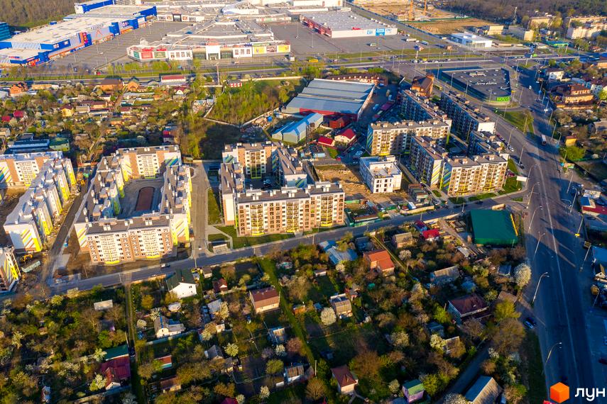 Аерофотозйомка житлового комплексу Welcome Home на вулиці Стеценка. Багатоповерхові будинки з яскравими фасадами розташовані навколо внутрішнього двору. Навколо комплексу зелені насадження та приватна забудова.