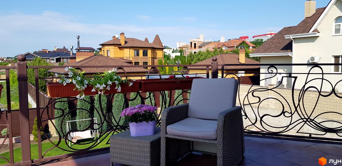Вид з балкону на будинки Котеджного містечка Флоринка. На передньому плані крісло з плетеного ротангу та квіти.
