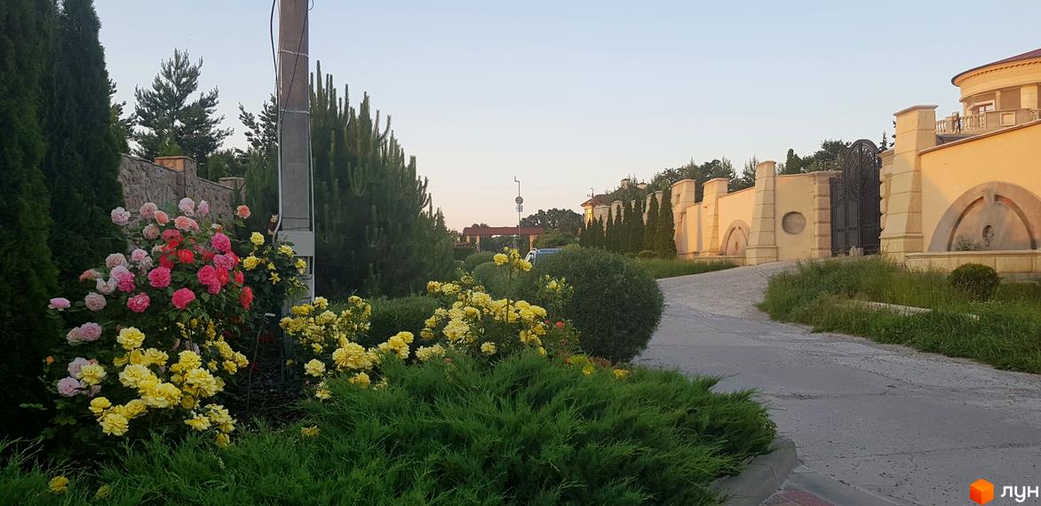 Вигляд на Котеджне містечко Флоринка з дорогою та зеленими насадженнями. На задньому плані видно паркан та будівлі.