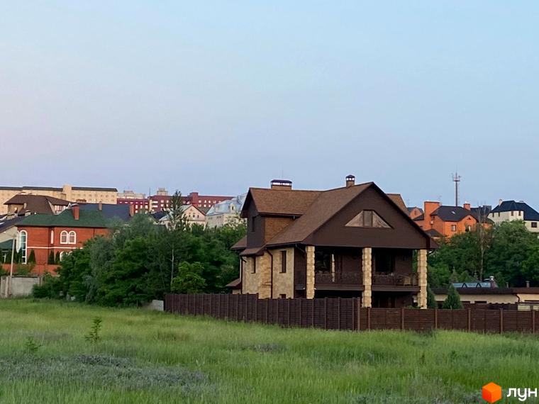 Фото будинку в Котеджному містечку Флоринка. Двоповерховий будинок з коричневим дахом та дерев'яним парканом на фоні зеленого поля.