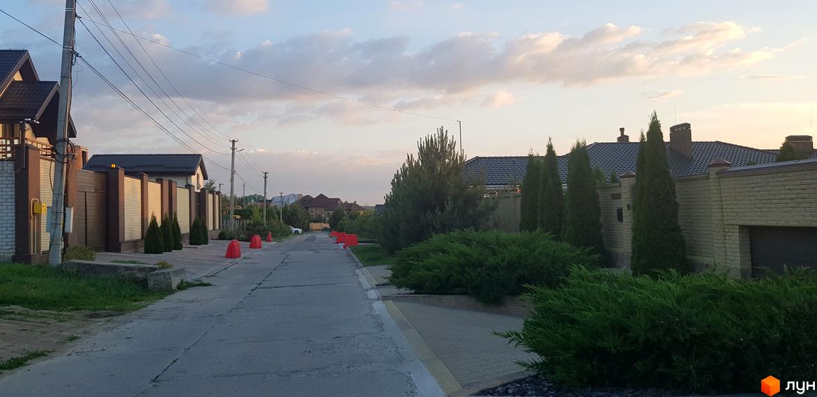 Фото вулиці в Котеджному містечку Флоринка. Вигляд на дорогу з будинками та зеленими насадженнями вздовж неї.