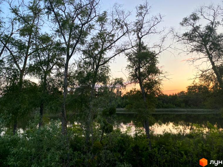 Зображення Житлового комплексу Флоринка на фоні заходу сонця та озера. На передньому плані дерева та зелені насадження.