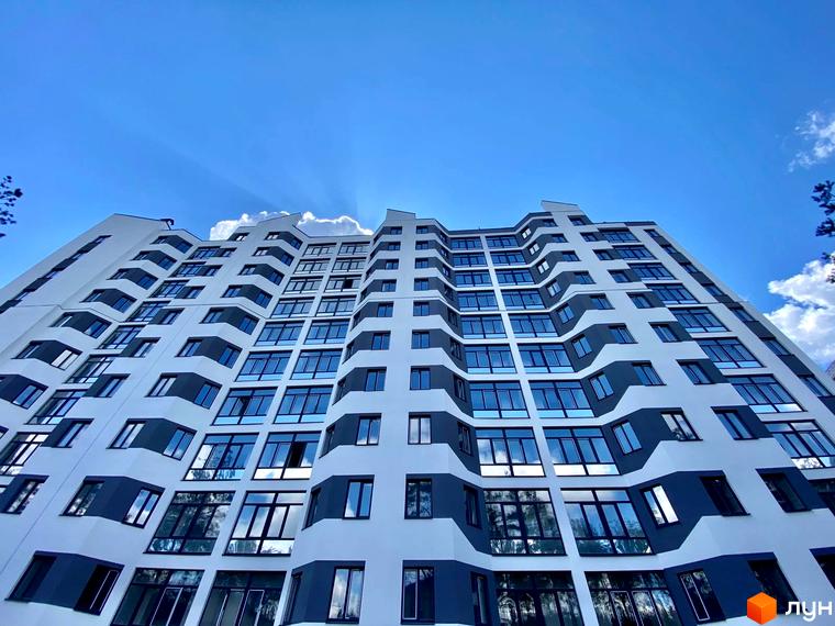 Новобудова ЖК Авіатор з вигнутим фасадом та великою кількістю вікон на фоні блакитного неба з хмарами. Зовнішній вигляд будівлі вражає своєю унікальною архітектурою.