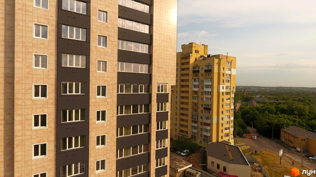 Житловий комплекс Столичний: фасади будинків з світлою плиткою та темними панелями, вікна, сусідні будівлі та зелена зона.