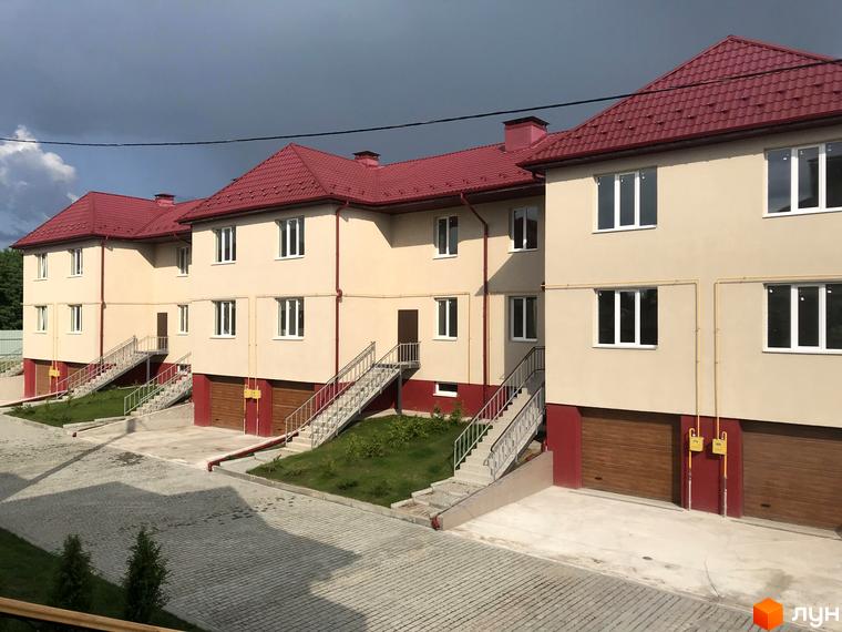 Котеджне містечко КМ Горобиновий маєток: двоповерхові будинки світло-бежевого кольору з червоними дахами, біля них сходи та гаражні ворота.