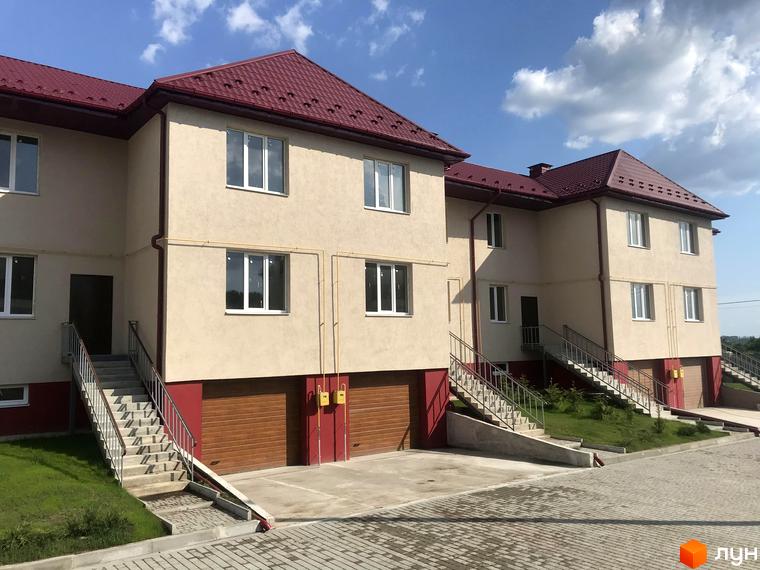 Зображення фасаду будинку в Котеджному містечку Горобиновий маєток з червоним дахом та гаражами на першому поверсі, з прилеглою територією.