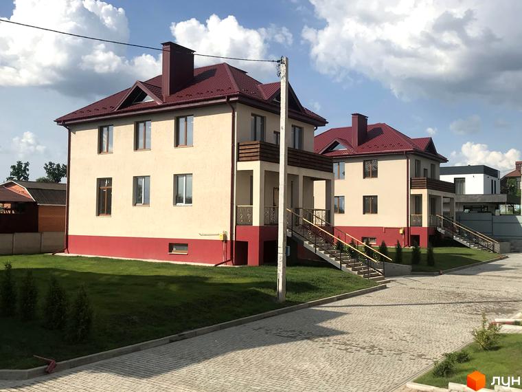 Котеджне містечко Горобиновий маєток: двоповерхові будинки світлого кольору з червоними дахами та цоколем. Перед будинками зелені газони, вимощена дорога та сходи з поручнями.
