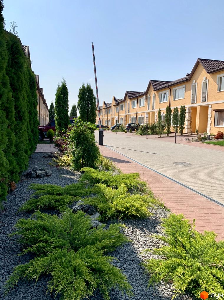 Фото таунхаусів Молодіжний XXI з фасадом жовтого кольору та коричневим дахом. Навколо будівель висаджені декоративні рослини та дерева.