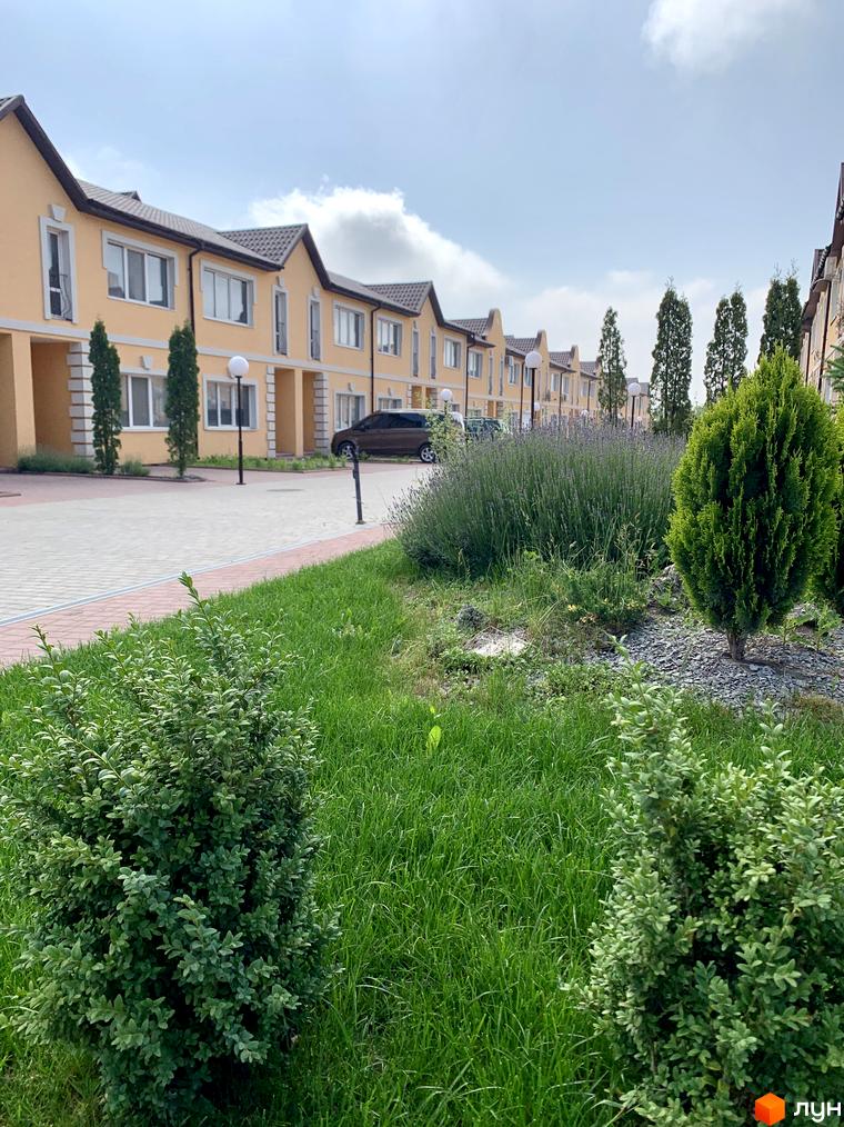 Зовнішній вигляд таунхаусів Молодіжний XXI з жовтими фасадами та коричневими дахами. На передньому плані зелені насадження та доглянутий газон.