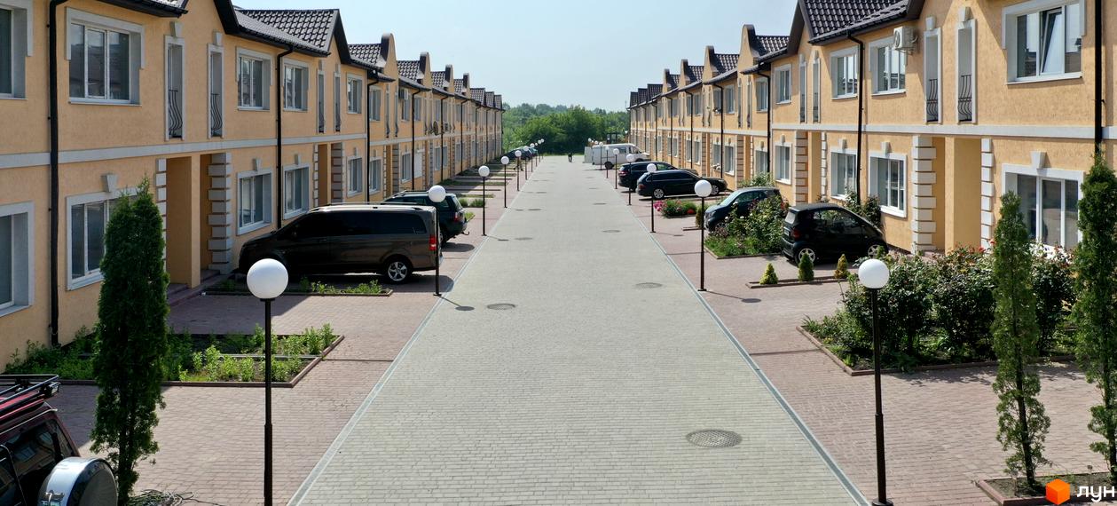 Зображення таунхаусів «Молодіжний XXI» з фасадом жовтого кольору. На території припарковані автомобілі та встановлені ліхтарі.