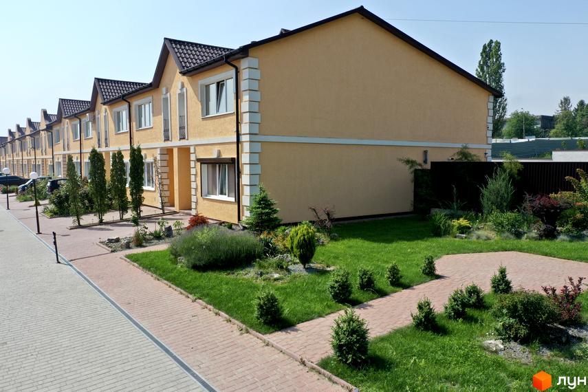 Зображення таунхаусів у Житловому комплексі „Молодіжний XXI“. Двоповерхові будинки з жовтими стінами та коричневими дахами, зелений газон і доріжки з бруківки.