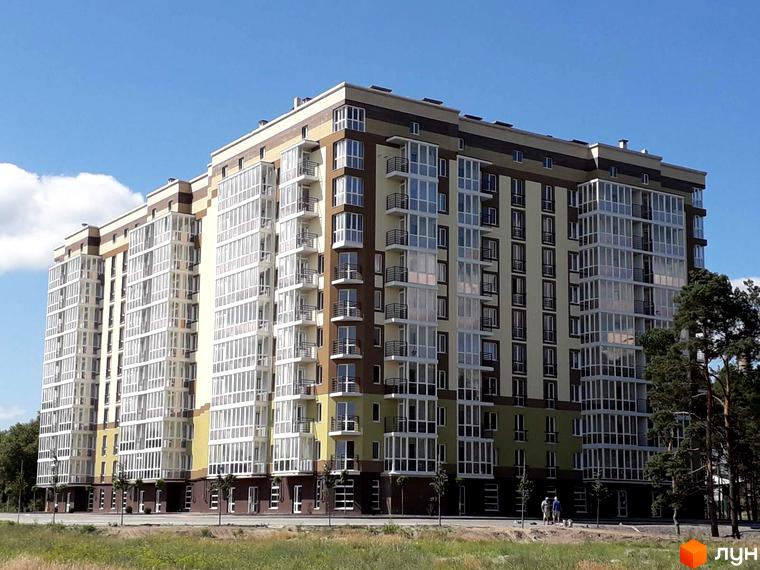 Житловий комплекс Oliva: багатоповерховий будинок з фасадом у відтінках коричневого, бежевого та зеленого, численними заскленими балконами. Поруч зелене поле та дерева.