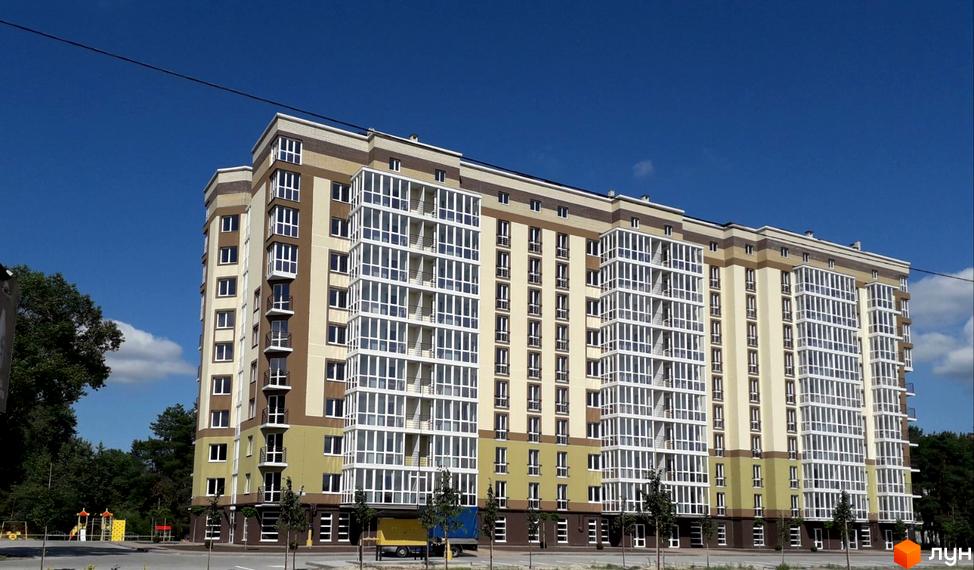 Багатоповерховий будинок Житлового комплексу Oliva з фасадом світлих відтінків та заскленими балконами. Поруч розташований дитячий майданчик та зелені насадження.