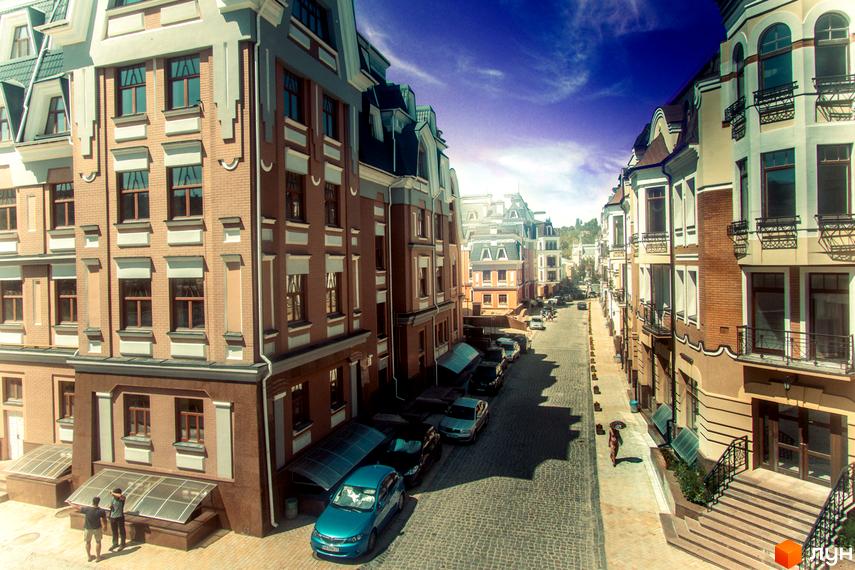 Зображення житлового комплексу Воздвиженка. Цегляні будинки з великою кількістю вікон, розташовані вздовж вулиці з бруківкою. На вулиці припарковані автомобілі.