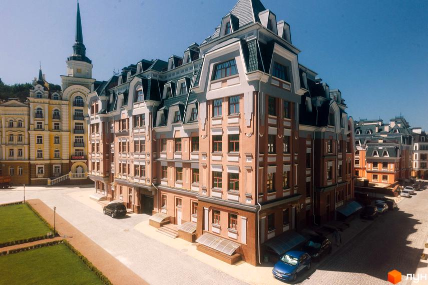 Зображення фасаду будинку ЖК Воздвиженка з цегляними стінами та мансардним дахом. Поруч розташована прибудинкова територія з бруківкою та газоном.