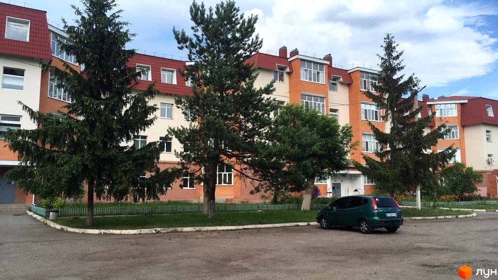 Будівля Житлового комплексу на вул. Гайок, 224б з похилими червоними дахами та світлими фасадами. Перед будинком зелений газон з деревами та парковка.