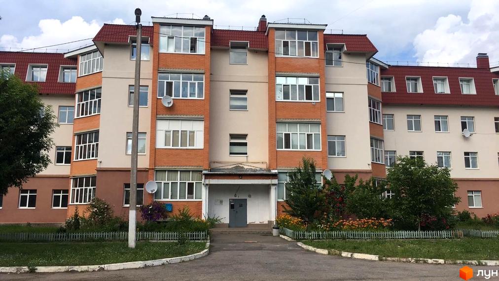 Зовнішній вигляд житлового комплексу вул. Гайок, 224б, з цегляними та світлими фасадами, червоним дахом та прибудинковою територією із зеленими насадженнями та парканом.