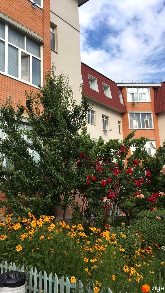 Житловий комплекс на вул. Гайок, 224б, з цегляним фасадом та червоним дахом. Перед будинком квітучий сад з жовтими та червоними квітами.