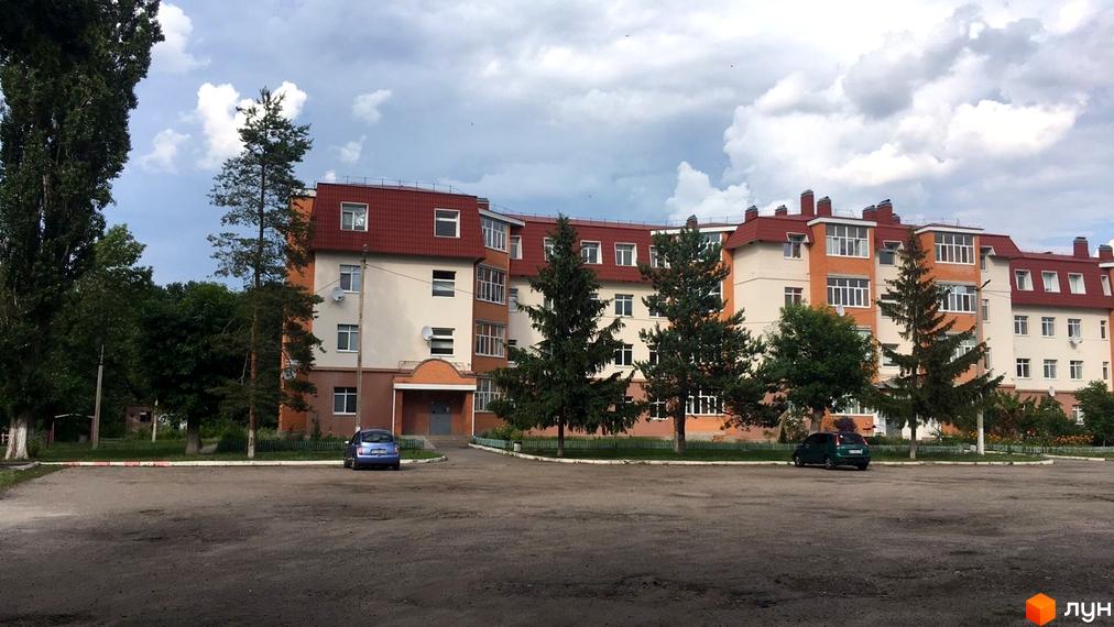 Житловий комплекс на вул. Гайок, 224б з червоним дахом та світлими фасадами. Перед будинком розташована простора прибудинкова територія з деревами та парковкою.