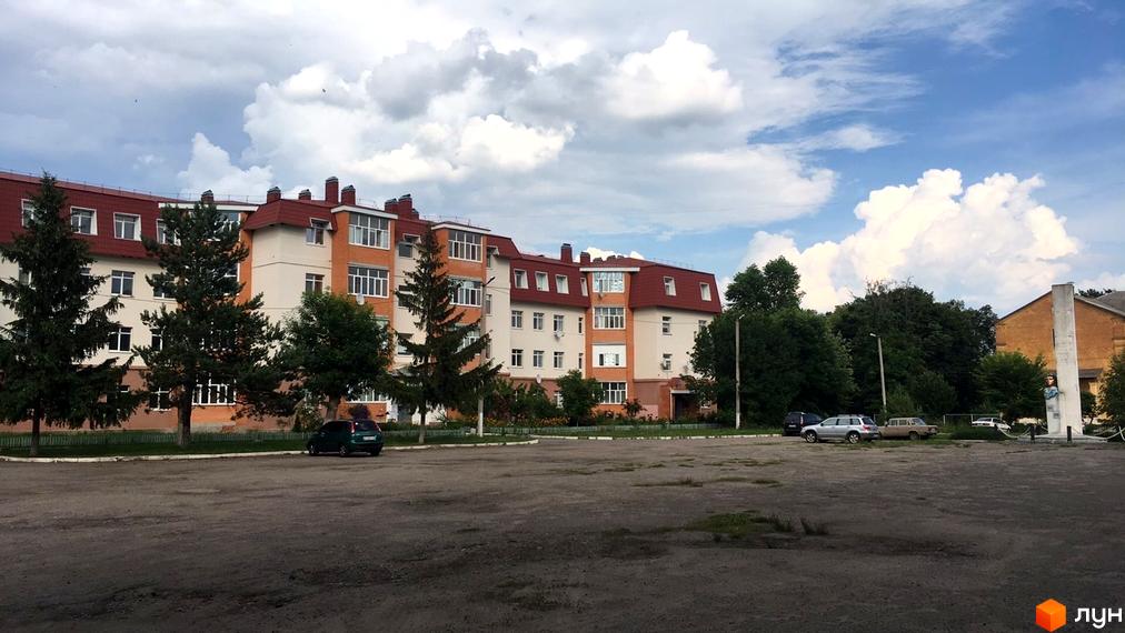 Новобудова на вул. Гайок, 224б: багатоповерховий будинок з червоним дахом, світлими стінами та прибудинковою територією з деревами.