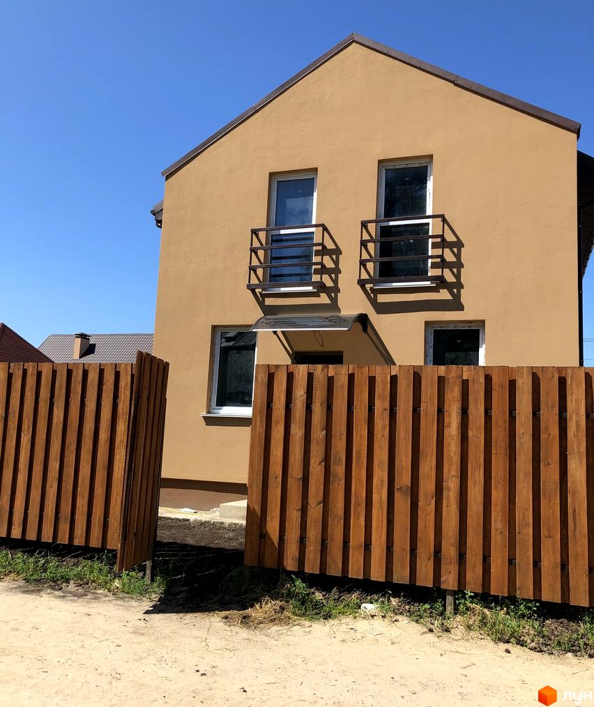 Котеджне містечко Sunny Village: двоповерховий будинок світло-коричневого кольору з темним дахом та вікнами з перилами. Перед ним дерев'яний паркан.