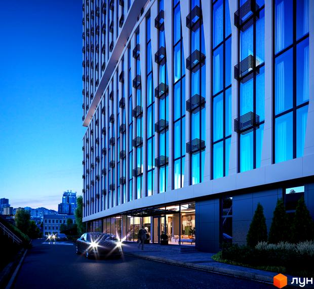 Апарт-комплекс Times з панорамними вікнами та декоративними елементами на фасаді, вечірній вид на вхідну групу та прибудинкову територію з дорогою та автомобілем.