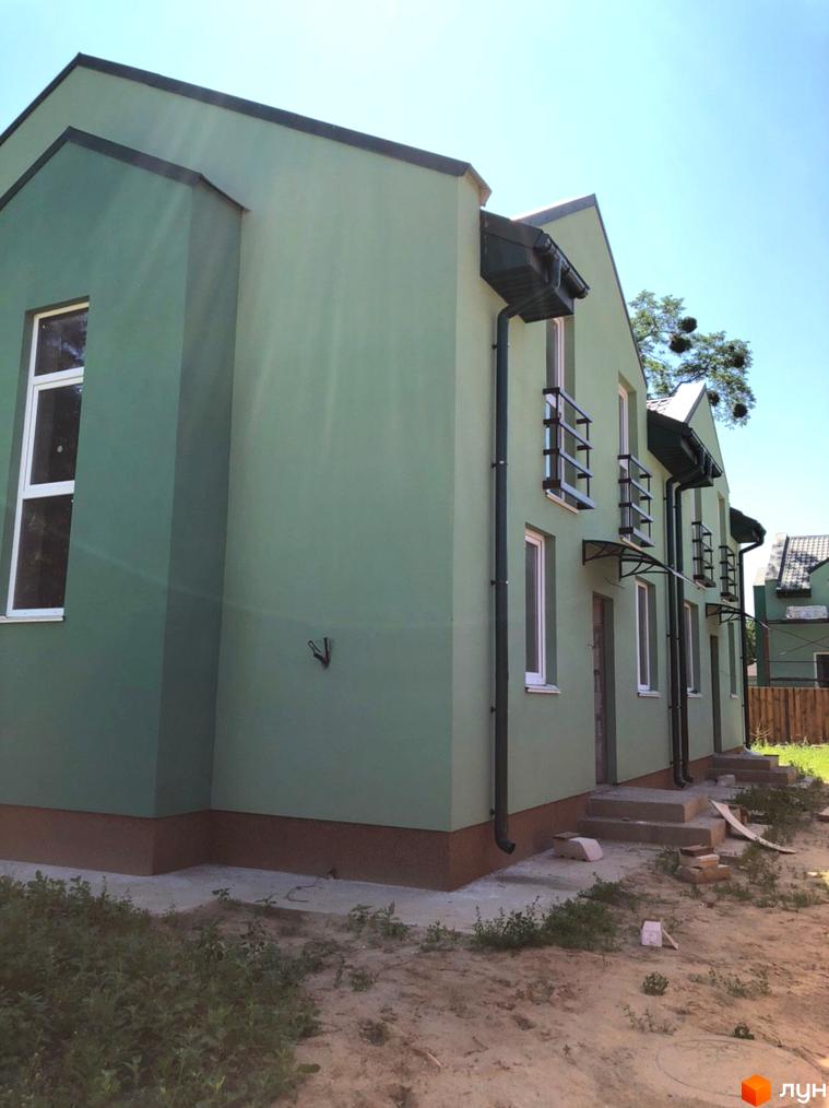 Ряд котеджів Котеджного містечка Sunny Village зі світло-зеленими фасадами, білими вікнами та темними водостоками. Прибудинкова територія з ґрунтом та поодинокою зеленню.