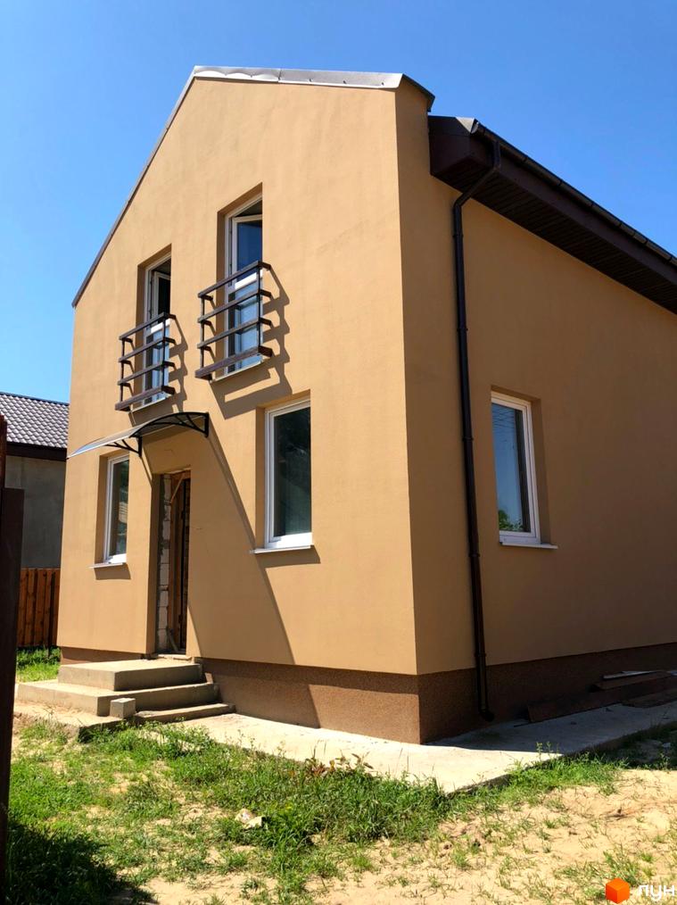 Котеджне містечко Sunny Village: світло-коричневий будинок з білими вікнами та темною водостічною системою. Перед будинком бетонні сходи та ділянка з травою.