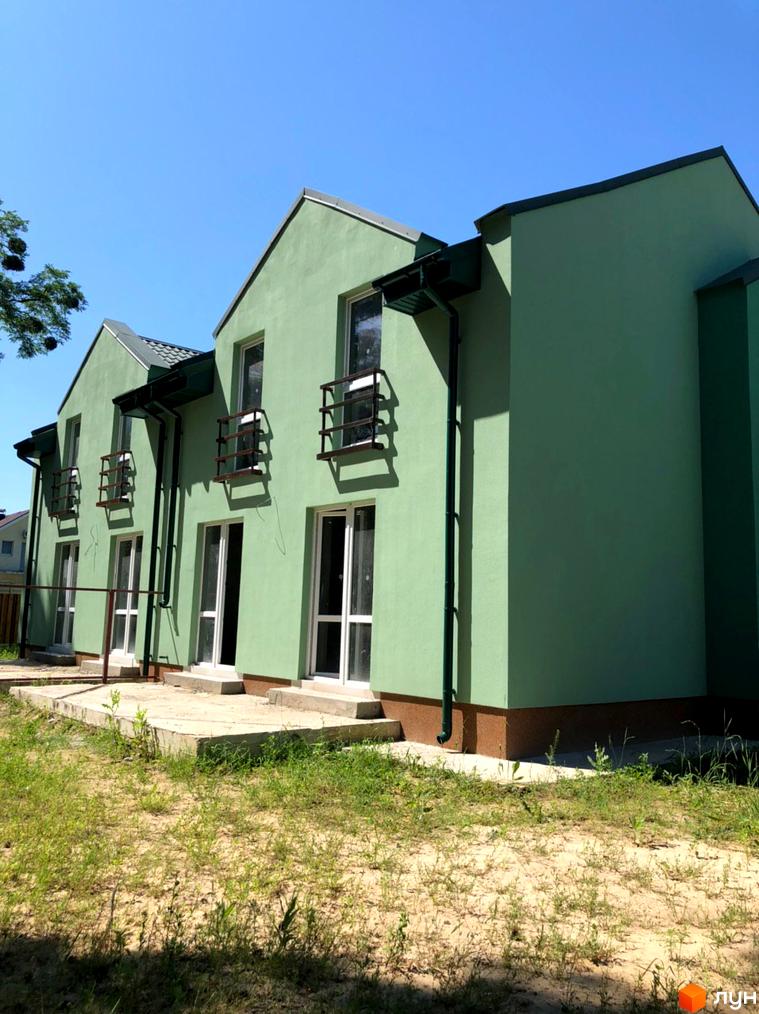 Фасад котеджного містечка Sunny Village: двоповерховий будинок салатового кольору з темним дахом та балконами. Прибудинкова територія з ґрунтом та травою.