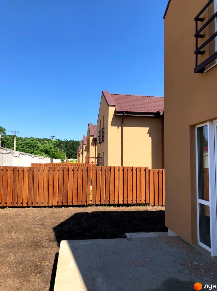 Будинки Котеджного містечка Sunny Village з коричневими дахами та світлими фасадами. Прибудинкова територія має дерев'яний паркан та підготовлений ґрунт.