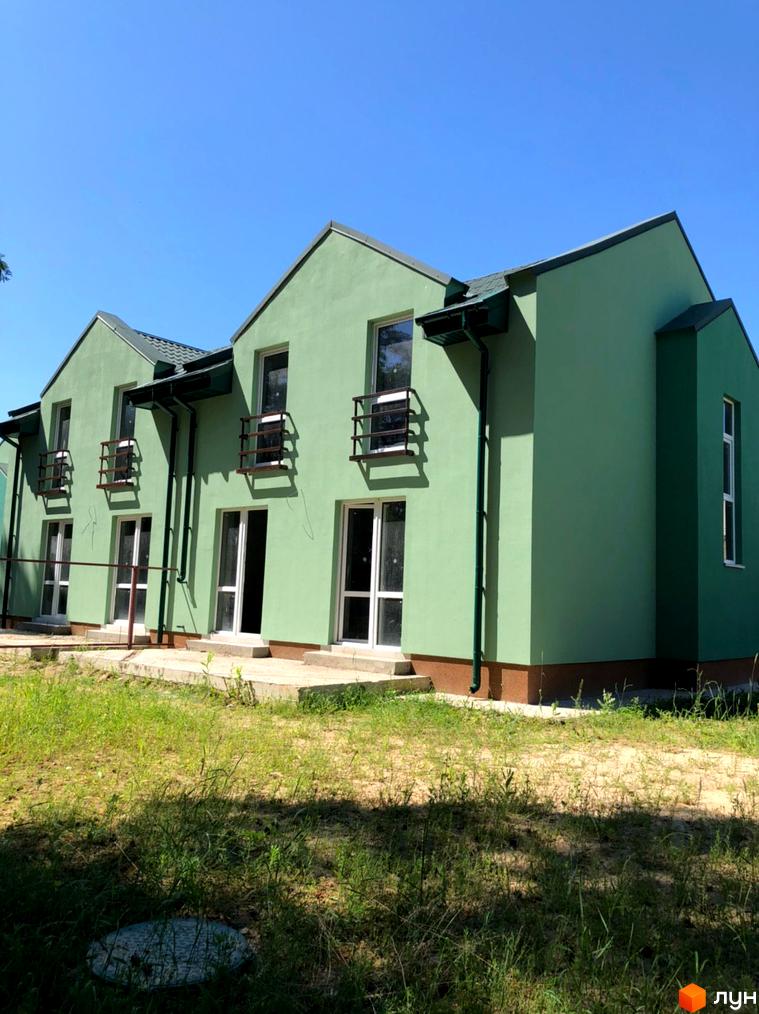 Котеджне містечко Sunny Village: двоповерхові будинки із зеленими фасадами, білими вікнами з огорожами та темними дахами. Прибудинкова територія з травою.