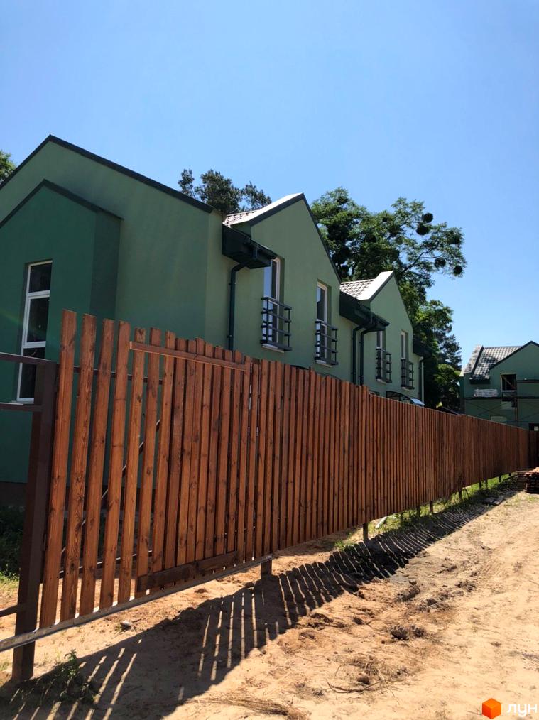 Ряд зелених будинків Котеджного містечка Sunny Village з темними дахами та дерев'яним парканом.