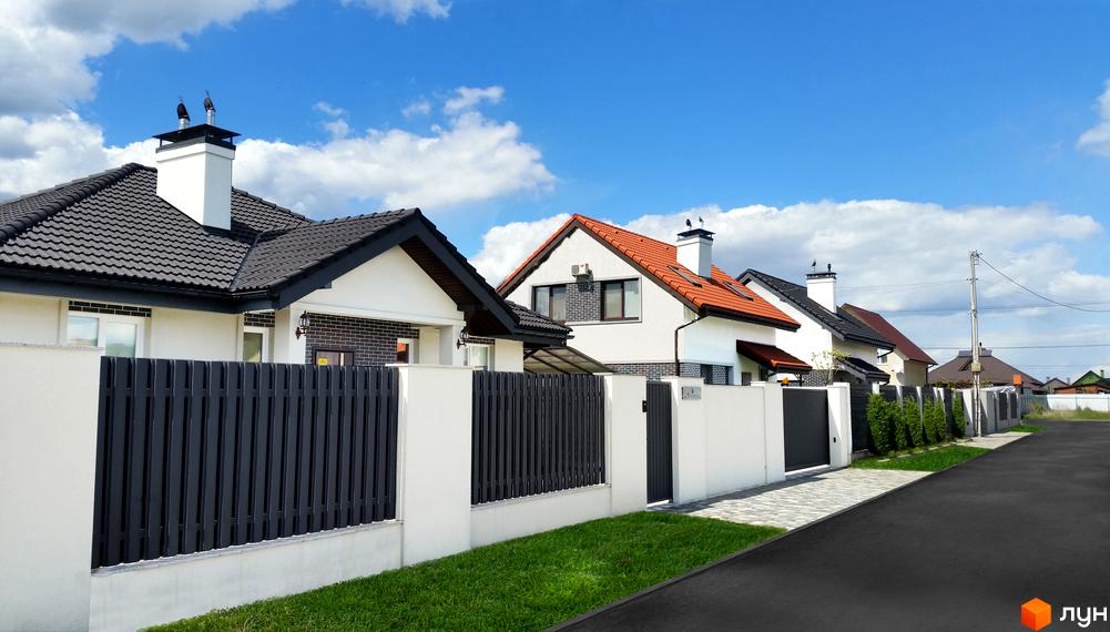Котеджне містечко КМ Сонячний: фасади будинків з червоною та чорною черепицею, білі стіни та сітчасті паркани. Територія комплексу з бруківкою та зеленими насадженнями.