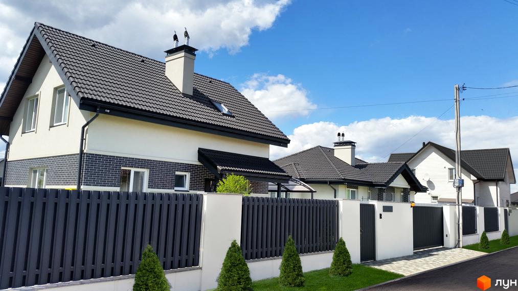 Котеджне містечко КМ Сонячний: фасади будинків з темним дахом, білою штукатуркою та цегляним оздобленням. Огороджена територія з доглянутим газоном та зеленими насадженнями.