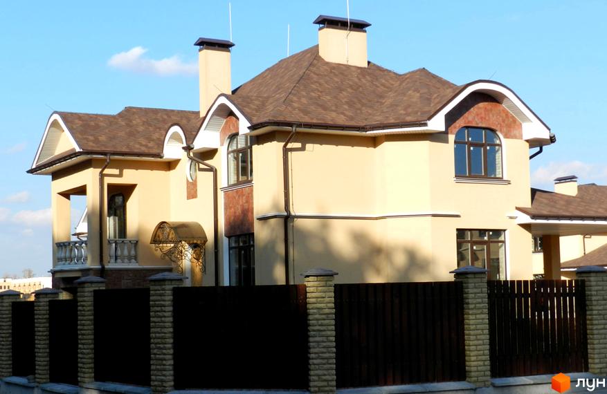 Зображення двоповерхового будинку в Котеджному містечку FEOFANIA COTTAGE з коричневим дахом та огорожею. На задньому плані видно блакитне небо.