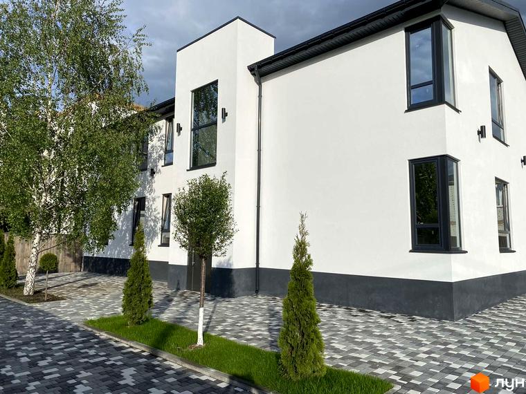 Новобудова ЖК Aura з білою фасадною штукатуркою та темною покрівлею. Прибудинкова територія з бруківкою та зеленими насадженнями.