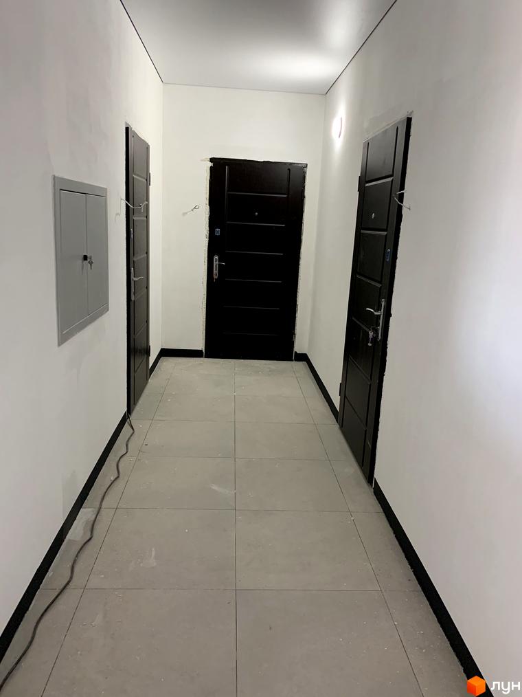 Коридор з дверима в житловому комплексі Aura. Відкритий простір з білими стінами та плитковою підлогою.