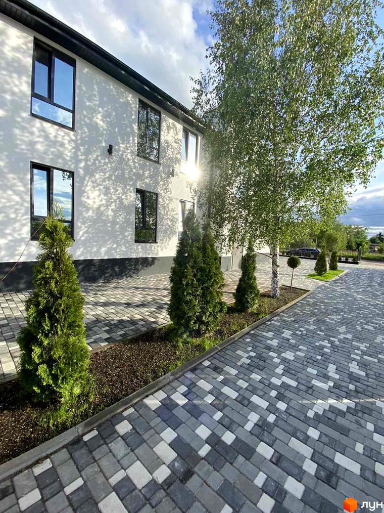 Зовнішній вигляд будинку ЖК Aura з панорамними вікнами та доглянутою прибудинковою територією з бруківкою та туями.