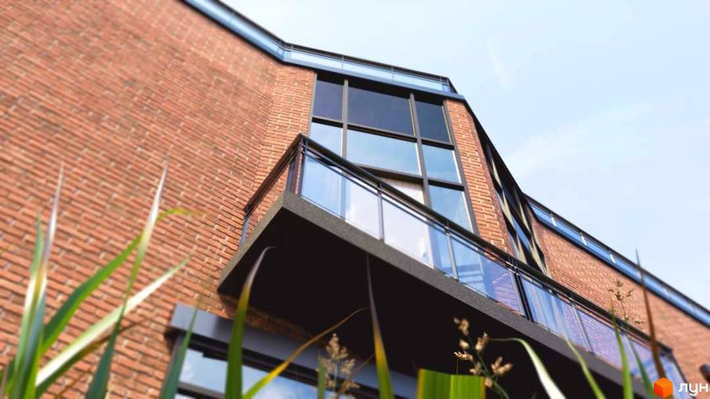 Житловий комплекс Європейський квартал: цегляний будинок з великими вікнами та балконом. На передньому плані зелені насадження.