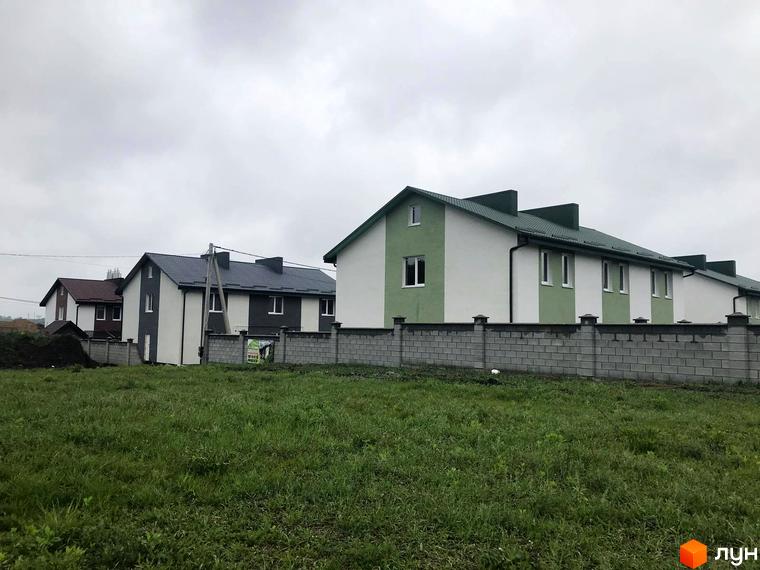 Таунхауси „Сонячна Долина“ з зеленим дахом та біло-зеленим фасадом. Перед будинками галявина з травою та сіра огорожа.