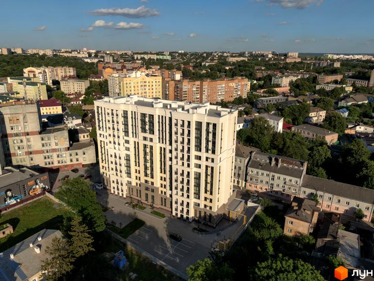 Висотна будівля ЖК Prestige Apartments з великою кількістю вікон. Поруч з будинком розташована прибудинкова територія з парковкою та зеленими насадженнями.