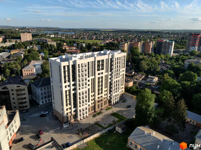 Висотна будівля ЖК Prestige Apartments з великою кількістю вікон на фоні міської забудови. На прибудинковій території є парковка та зелені насадження.