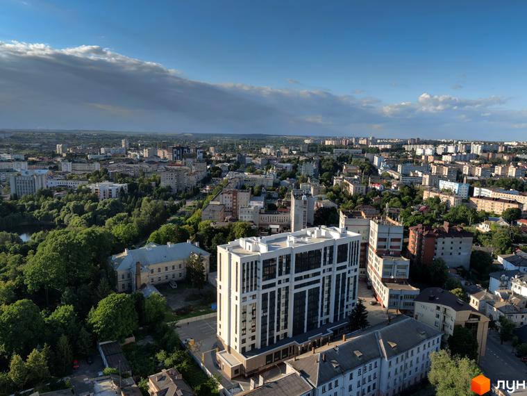 Висотна будівля житлового комплексу Prestige Apartments на фоні міської забудови. Навколо будинку зелені насадження та прибудинкова територія.
