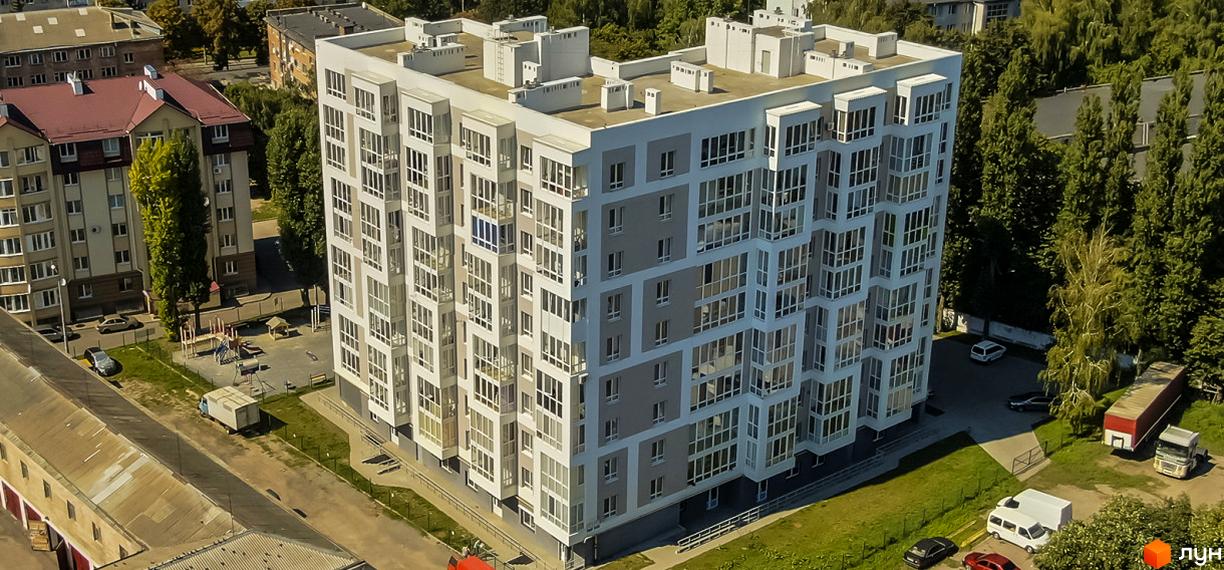 Зовнішній вигляд багатоповерхового житлового комплексу на вул. Володимира Стельмаха (Курчатова), 1б, з численними вікнами та балконами. На прибудинковій території видно дитячий майданчик та припарковані автомобілі.
