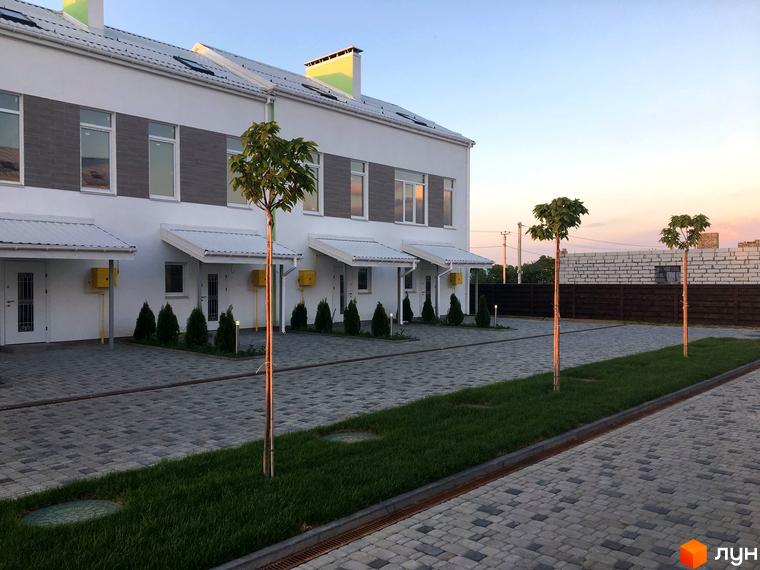 Таунхауси Apple House з білими фасадами та сірими елементами на фасаді, перед будинками розташована бруківка та зелені насадження.