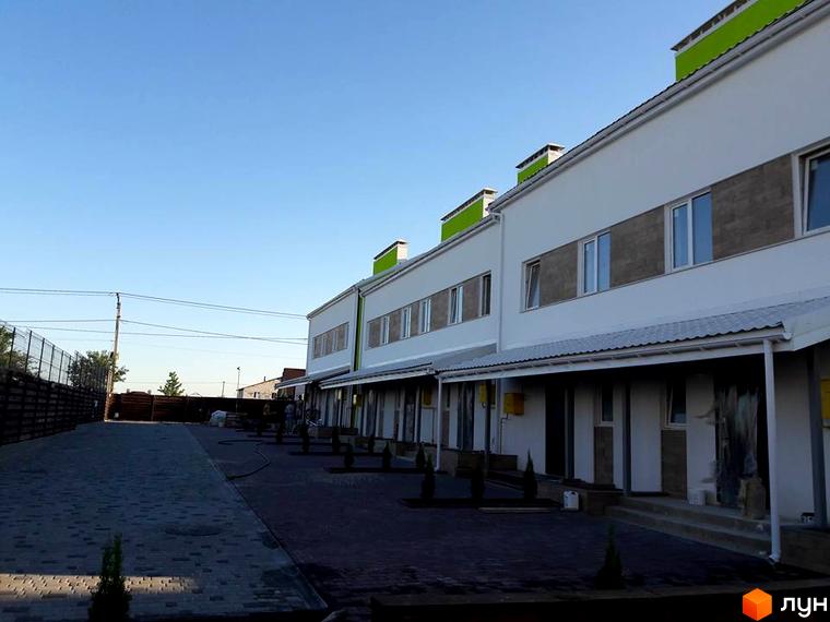 Таунхауси „Apple House“: білі будинки з зеленими акцентами та сірими вставками на фасаді. Прибудинкова територія вимощена бруківкою з молодими насадженнями.