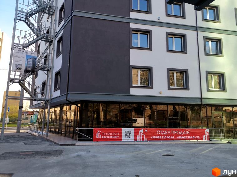 Зовнішній вигляд будинку Житловий комплекс Защитник з вікнами та пожежною драбиною. Перед будинком банер Turkish Development.