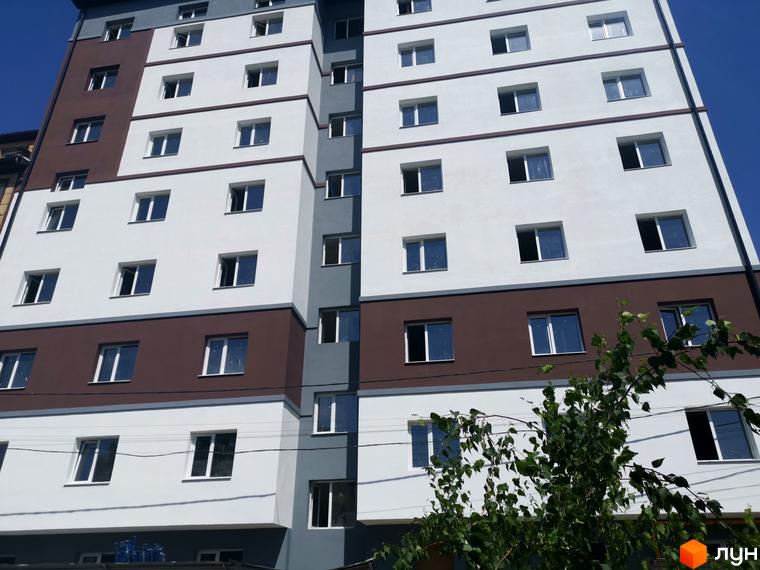 Фасад житлового комплексу Благовест з білими та коричневими елементами, великою кількістю вікон та зеленню на передньому плані.